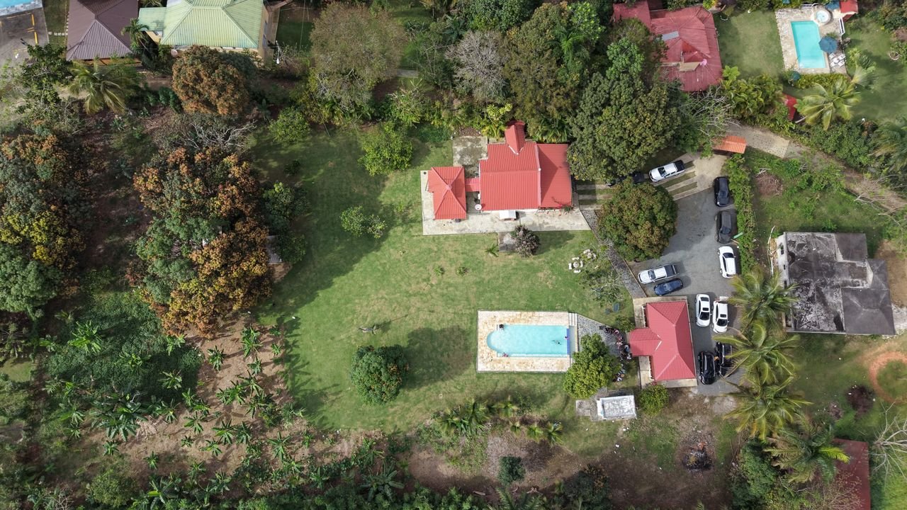 Bird's-eye view of a lush property with red-roofed buildings and swimming pools, surrounded by tropical greenery.